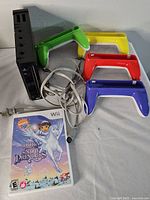 Photo showing black Nintendo Wii console with power and sensor cables, four plastic Wii Wheel accessories in green, yellow, red, and blue, and 'Dora Saves the Snow Princess' Wii game case.