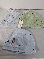 Three baby beanies, two light blue with Tigger embroidery and one light green with Winnie The Pooh embroidery, all with polka dot patterns and tags visible.