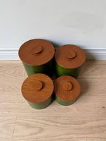 Four vintage stackable canisters in green with teak wood lids arranged on floor, top view showing lids.