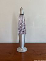 Full side view of the glitter lava lamp showing its silver base and top and clear liquid with silver glitter inside.
