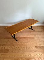 Side angle view of the mid-century boat shaped coffee table highlighting the warm wood grain surface and black metal legs.