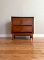 Front view of the mid-century nightstand showing the two drawers with decorative carved handles.