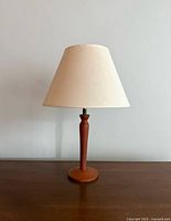 Front view of the mid-century teak table lamp with beige shade on wooden surface against white wall.