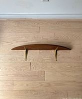 Top view showing natural wood semi-circle shelf with two brass-colored metal mounting brackets.