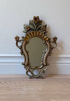 Full front view of the small vintage mirror showing floral and scroll metal frame with a gold and greenish finish.