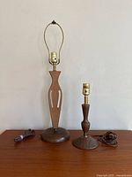 Photo showing two vintage wooden table lamps side by side without shades or bulbs, placed on wooden surface.