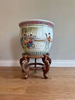Frontal view of the vintage Chinese porcelain planter on wooden stand, showing detailed hand-painted scene of women in garden outdoors and overall structure.