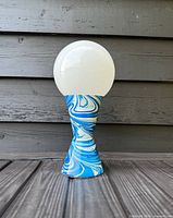 Full view of vintage table lamp with swirl blue and white base and white glass globe shade.