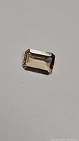 Photo showing emerald cut champagne colored morganite gemstone on a neutral background.