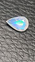 Pear-shaped faceted opal gemstone with vibrant rainbow play of colors on black textured background, showing clean and clear qualities.