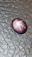 Close-up of the oval cabochon natural star ruby showing six-ray star effect on a textured dark surface.