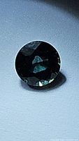 Close-up photo of round faceted dark blue sapphire gemstone showing facets and color under light.