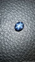 Photo of single oval cabochon natural blue star sapphire on textured black background showing the 6-ray star asterism effect under light.