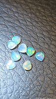 Eight small natural teardrop cut Ethiopian opal gemstones positioned on a black textured surface. Gems show strong multi-color play of color and translucence.