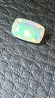 Cushion cut natural Ethiopian opal showing subtle green and yellow flashes on textured black background.