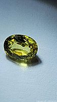 Close-up image of oval natural yellow sapphire gemstone with high luster and blue undertone on white surface.