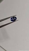 Close-up photo of the oval cut natural tanzanite gemstone held by tweezers, showing intense blue-violet color and sparkle.