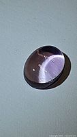 Close-up photo of a single oval cabochon Brazilian amethyst gemstone showing its purple color and surface polish.
