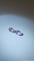Photo of two oval cut natural purple amethyst gemstones, matched pair shown on white surface with light highlighting facets and color.