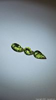Three natural apple green peridot gemstones on a white background, showing oval, round, and pear cut shapes and their clarity and color.