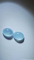 Pair of oval cabochon cut natural untreated aquamarine gemstones with strong blue color, shown against white background under directional light.