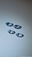 Four pear-shaped sky blue topaz gemstones placed on a gray background showing the shape, size and clarity of the stones.