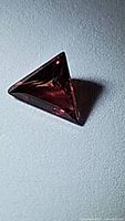 Close-up photo of a natural fancy step trillion cut pink orange sapphire showing its triangular shape and intense color.