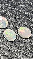 Three oval checkerboard cut Ethiopian opals on a textured black surface showing their iridescent play of colors