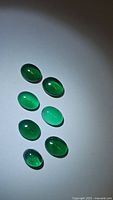 Seven natural oval cabochon green onyx gemstones on white background showing color and clarity