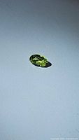 Oval cut natural apple green peridot gemstone, approx 6x4mm, shown against white background from a side angle, highlighting the facets and color.