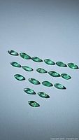 Collection of 18 marquise-cut emerald gemstones arranged on white background.