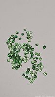 Natural tsavorite garnet gemstones scattered on a neutral background showing their green color and round cut faceting.