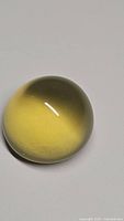 Oval cabochon cut natural lemon citrine gemstone with deep rich yellow color on white background showing smooth polished surface.