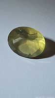 Photo of an oval cut lemon citrine gemstone showing pale yellow-green color and multiple facets under light