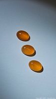 Three oval mandarin carnelian cabochon gemstones on a white background, showing their rich orange hue and polished surfaces.