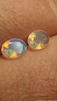 Close-up photo of two oval cut Ethiopian opal gemstones showing play-of-color on a textured background.