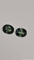 Two oval-shaped green sapphires with blue and yellow undertones placed on a light-colored surface.