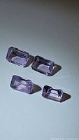 Four natural purple amethyst gemstones with emerald cut, shown from above on a white surface.