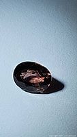 Oval faceted sapphire shown with dark background lighting, displaying a deep purplish hue.