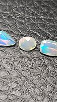 Three natural Ethiopian opals placed side-by-side on textured black surface, showing their different cuts and opalescent flashes.