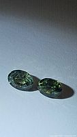 Two oval cut natural green sapphires on a white background showing color and clarity.