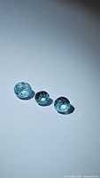 Three natural seafoam blue zircon gemstones shown on a plain surface with light reflection showcasing their faceting and color.