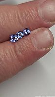 Three natural calibrated cushion cut tanzanite stones held on fingers showing size and color.
