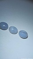 Three oval cabochon gemstones of white crazy lace agate laid out on a flat surface with visible intricate lace-like white and grey patterns, photo taken for detailed view of lot contents