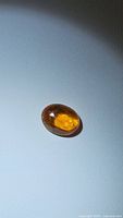 Close-up photo showing the oval cabochon cut sapphire gemstone with deep yellow-orange color and internal inclusions.