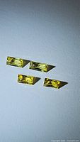 Four baguette-cut natural canary yellow sapphires arranged on a flat surface showing their yellow color and clarity.