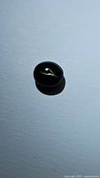 Oval dark green catseye augite gemstone showing distinct catseye light reflection effect on smooth polished surface.