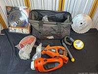 Black & Decker tool bag with electric tools, hose, flashlight, and saw blades spread out on dark surface