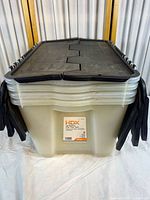 Stack of four clear plastic storage totes with black flip top lids stacked one inside the other.