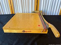 Full view of the Ingento guillotine paper cutter showing the wooden base with grid and metal cutting arm.